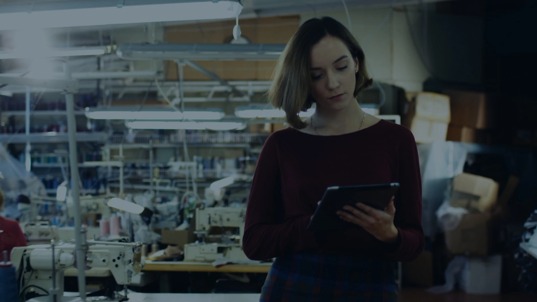 A woman uses a tablet among sewing machines in a garment workshop.
