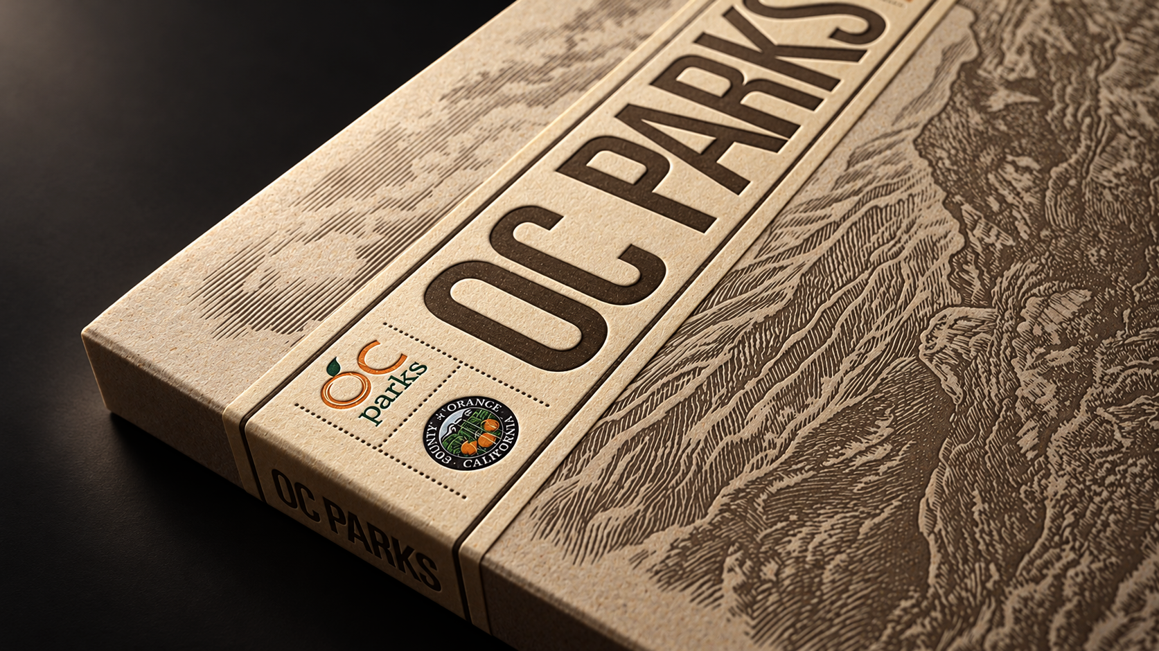Close-up of a textured OC Parks publication cover with landscape illustrations, park branding, and the Orange County seal in warm light.